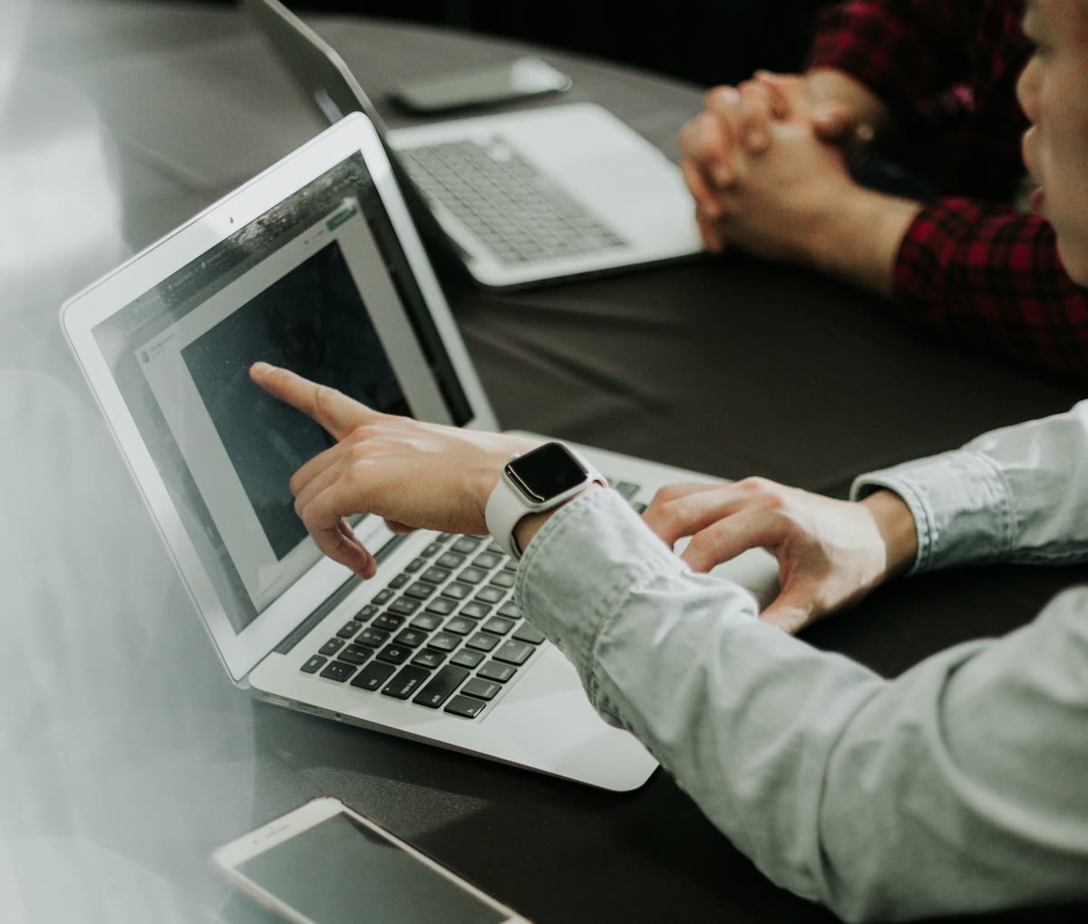 Une personne montre un point précis sur l'écran d'un ordinateur portable, à côté d'un collègue, autour d'une table de travail
