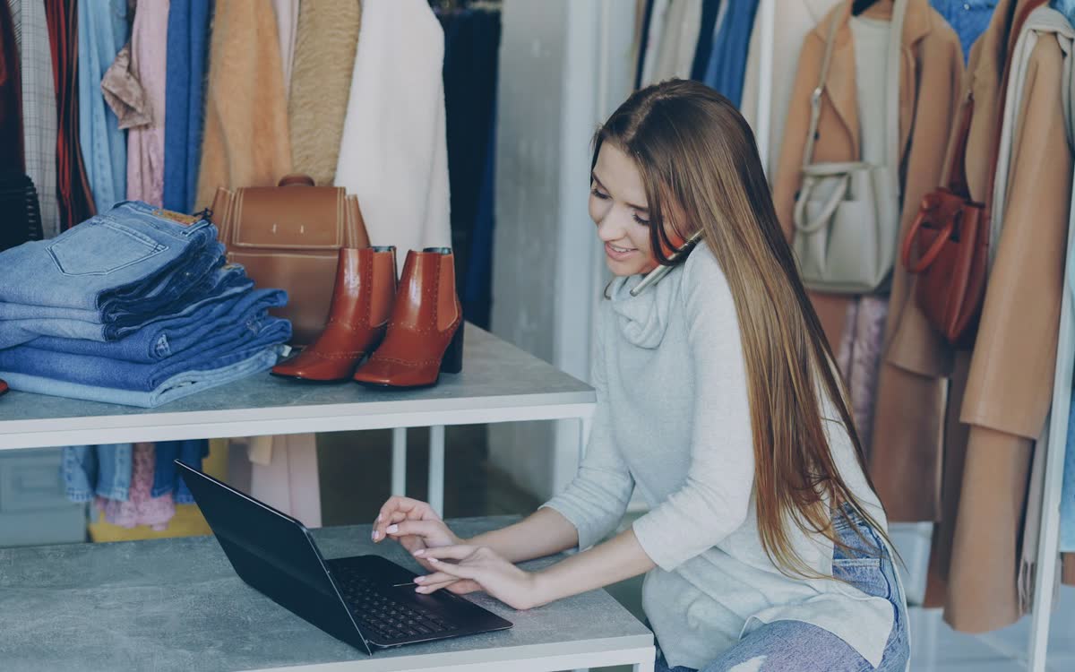 Une commerçante travaille sur son ordinateur au milieu des vêtements de sa boutique